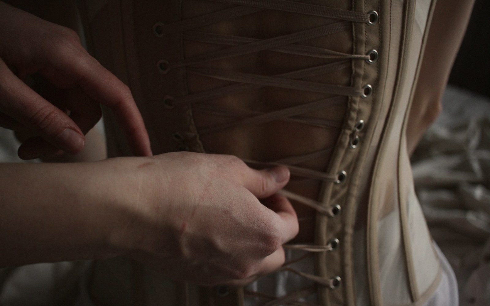 Hands lacing up the back of a corset through metal eyelets