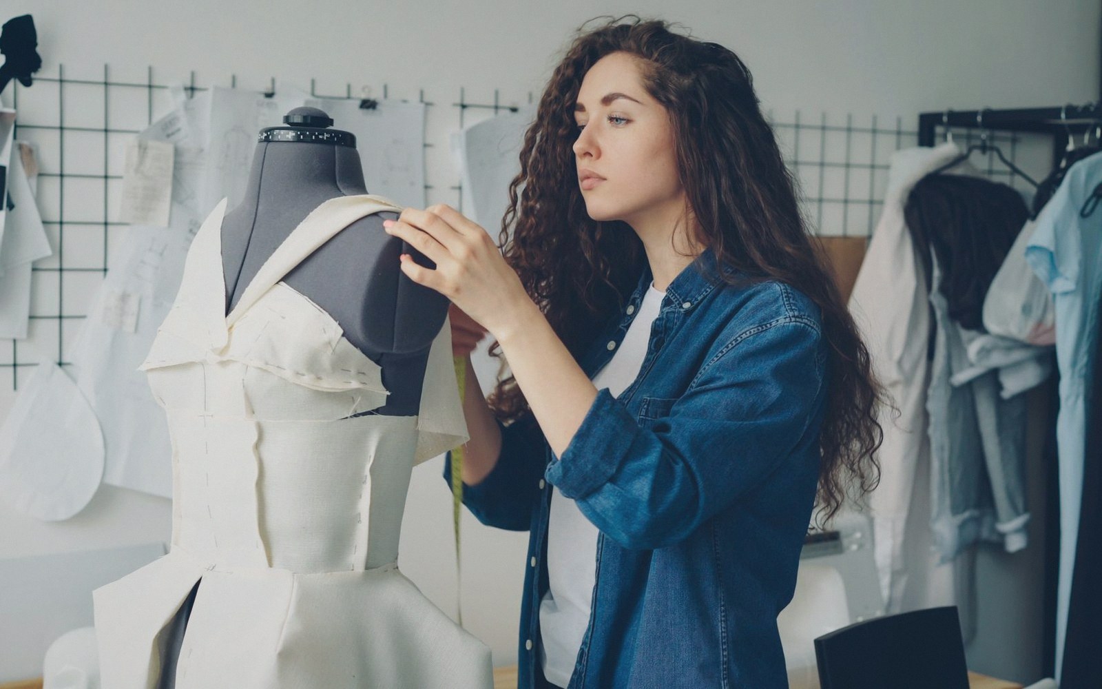 A designer pins fabric on a dress form in a studio surrounded by sketches