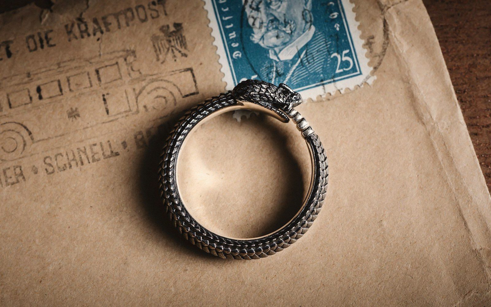 A snake-shaped ouroboros ring resting on an old envelope with a postage stamp