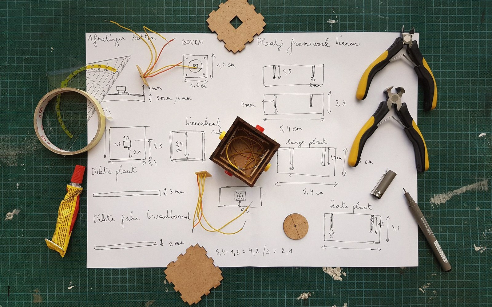 Hand-drawn wiring diagrams surround a small wooden box with wire mesh, pliers, and glue nearby