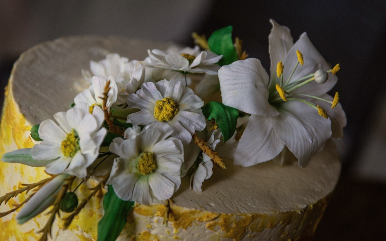 White sugar flowers and green leaves decorating the top of a frosted cake