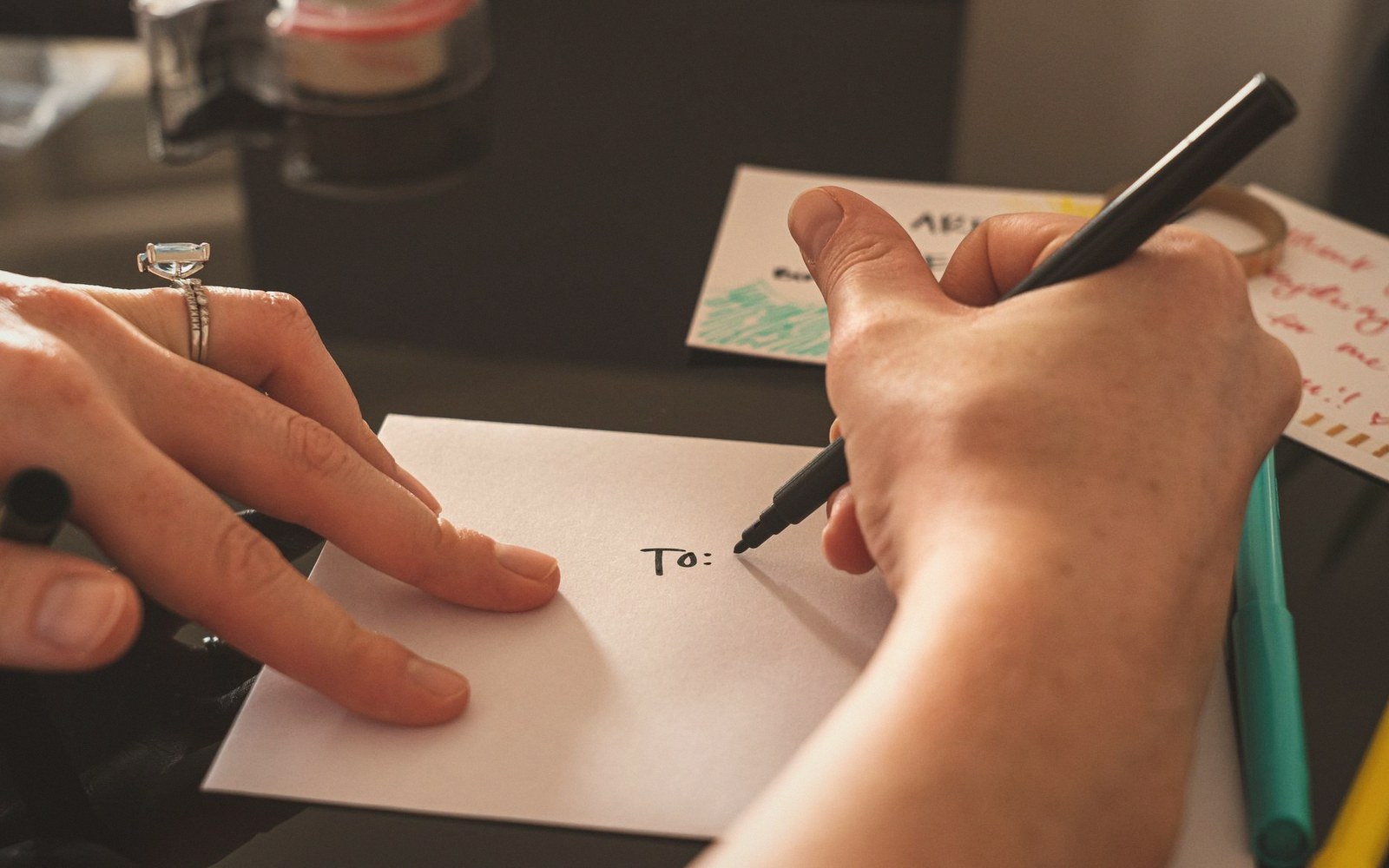 A hand holding an envelope steady while another writes "To:" on it with a marker