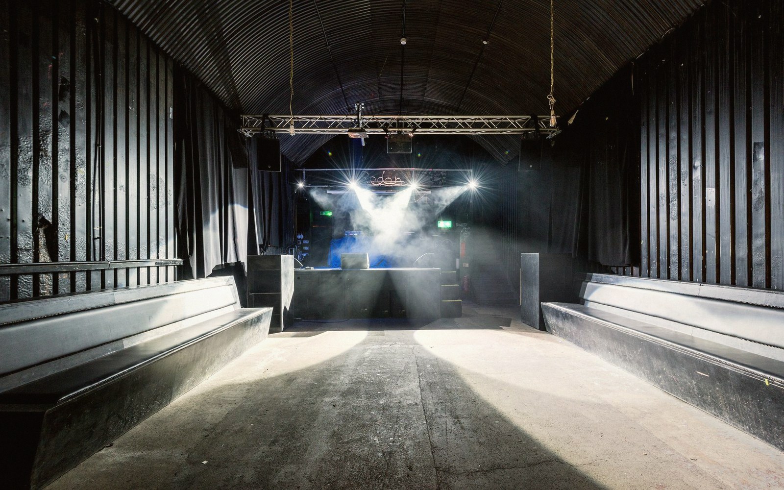 Empty music venue with arched ceiling, stage lighting beams cutting through haze