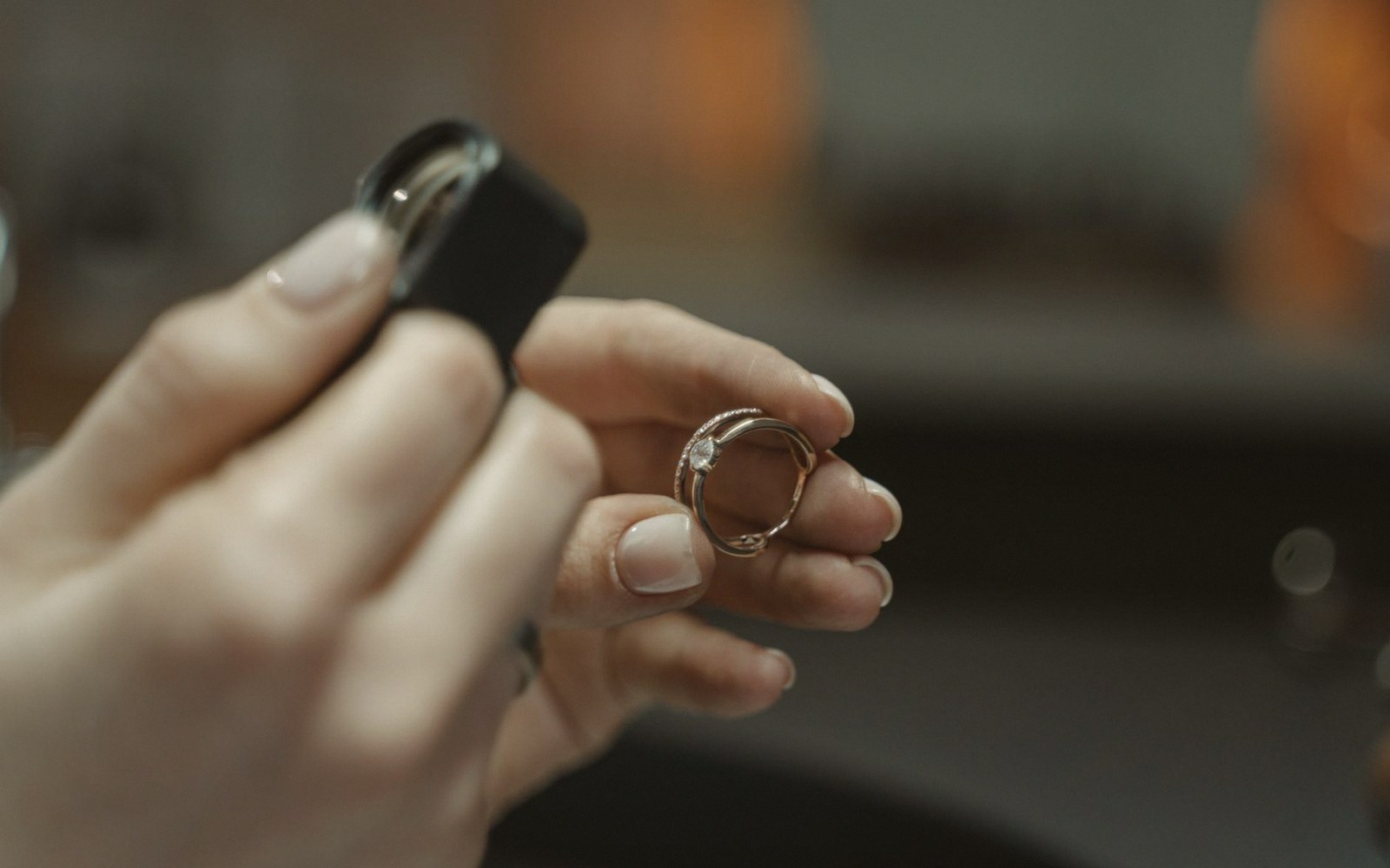 Hands holding a diamond ring alongside a small jeweler's loupe for inspection